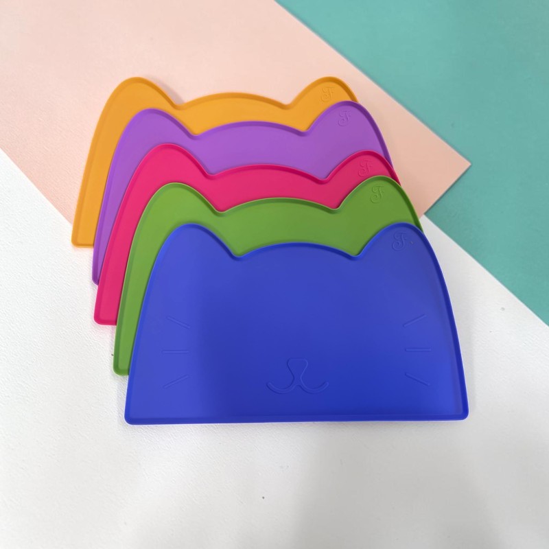 Fünf bunte, stapelbare Unterlagen in Katzenform, von vorn nach hinten in Blau, Grün, Pink, Lila und Orange. Mit eingeprägtem Katzengesicht samt Nase, Schnurrhaaren und kleinen Ohrsymbolen, auf modernem Hintergrund.